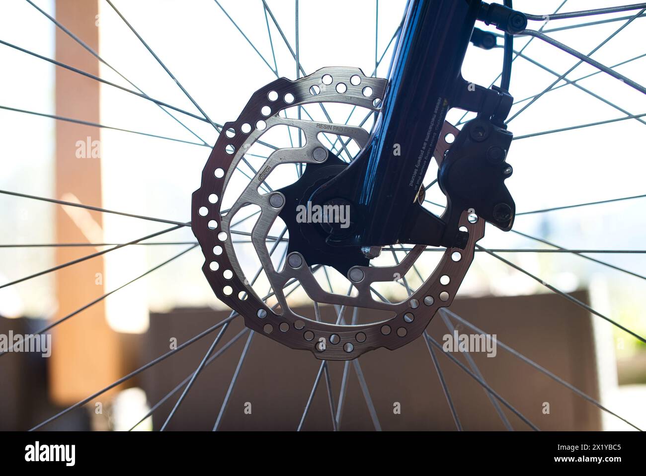 Nahaufnahme des Vorderrads eines E-Bikes mit einer Bremsscheibe aus Edelstahl, einem Bremssattel und einem Abschnitt der dunkelblauen Hochglanzgabel. Stockfoto