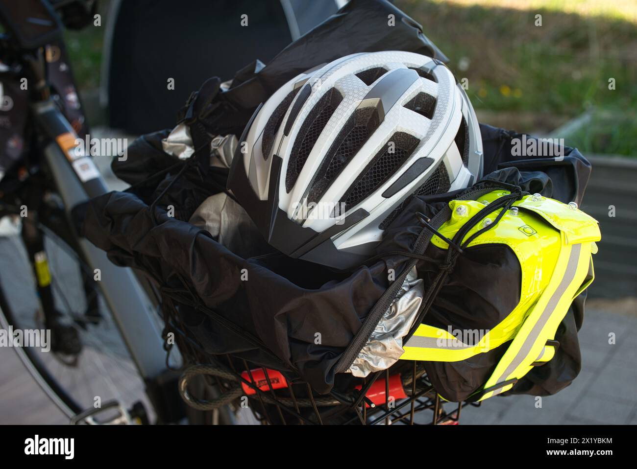 Rückansicht eines E-Bikes mit dem Fahrradgepäckträger, der einen Fahrradhelm, eine reflektierende Weste, ein Fahrradschloss, eine Regenabdeckung und eine Plane enthält. In Th Stockfoto