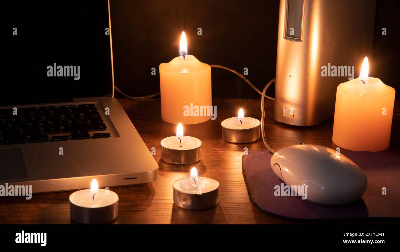 Verdunkelungskonzept, 6 beleuchtete Kerzen beleuchten den Arbeitsbereich mit einem Laptop auf schwarzem Hintergrund Stockfoto