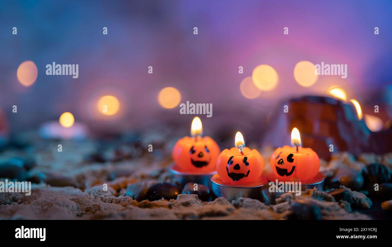 Halloween-Hintergrund, 3 Kerzen in Kürbisform im Vordergrund vor einem unscharfen Hintergrund mit gelben Lichtern Stockfoto