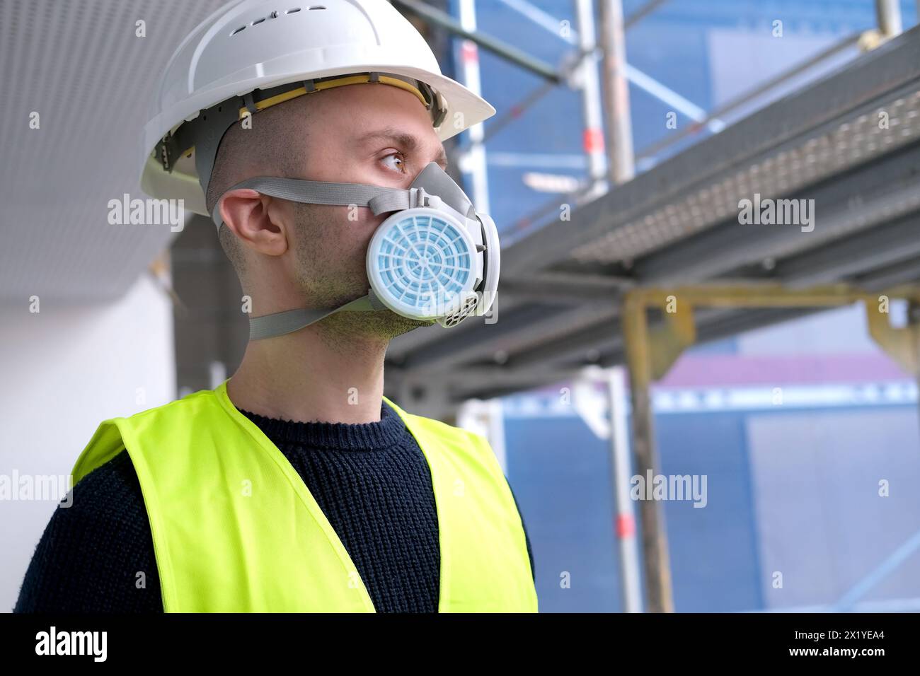 Junger männlicher Baumeister, Ingenieur oder Architekt in weißem Schutzhelm und Atemschutzmaske während der Inspektion auf der Baustelle, Konzept des Monitos Stockfoto