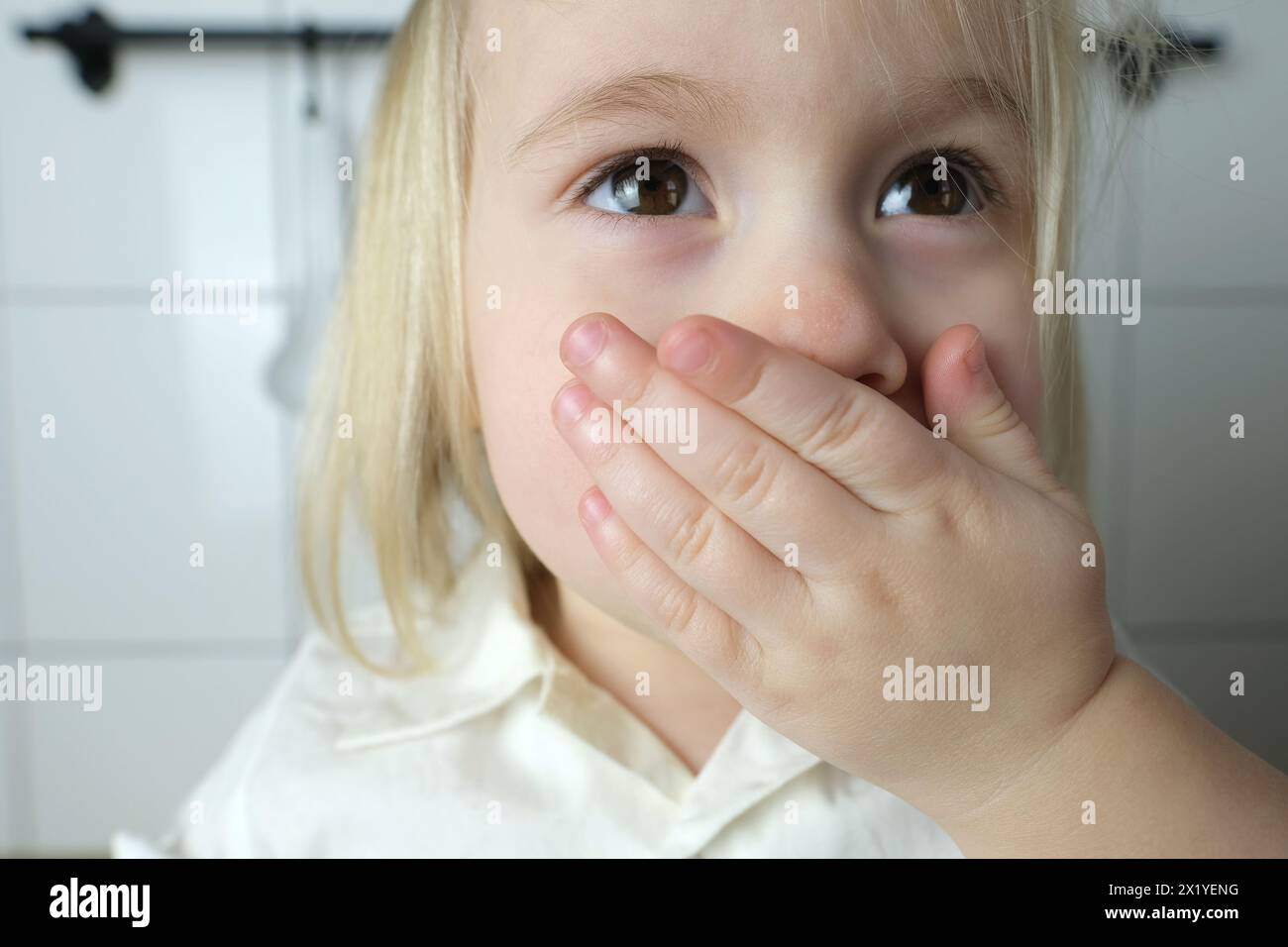 Kleines Kind, Baby, blondes Mädchen bedeckte ihren Mund mit ihrer Hand, das Konzept der Erziehung, Bestrafung für schlechte Worte, Kinderwitze, necken Stockfoto