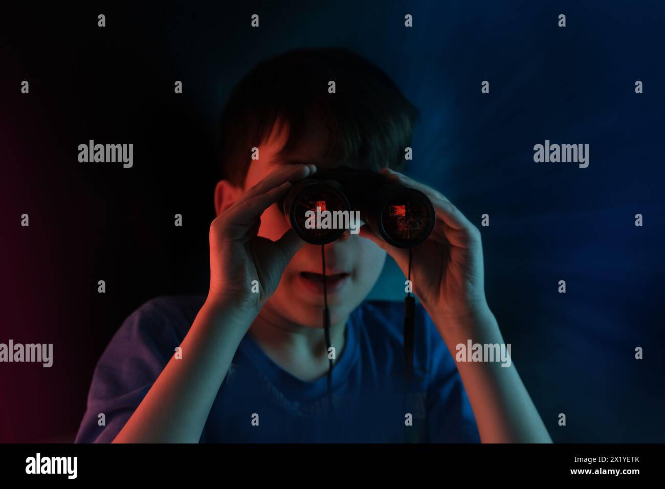 Junge, Typ 7-9 Jahre alt, Stalker schaut durch ein schwarzes Fernglas im Dunkeln, spioniert, spürt Geheimnisse des Privatlebens auf, das Konzept der Überwachung Stockfoto