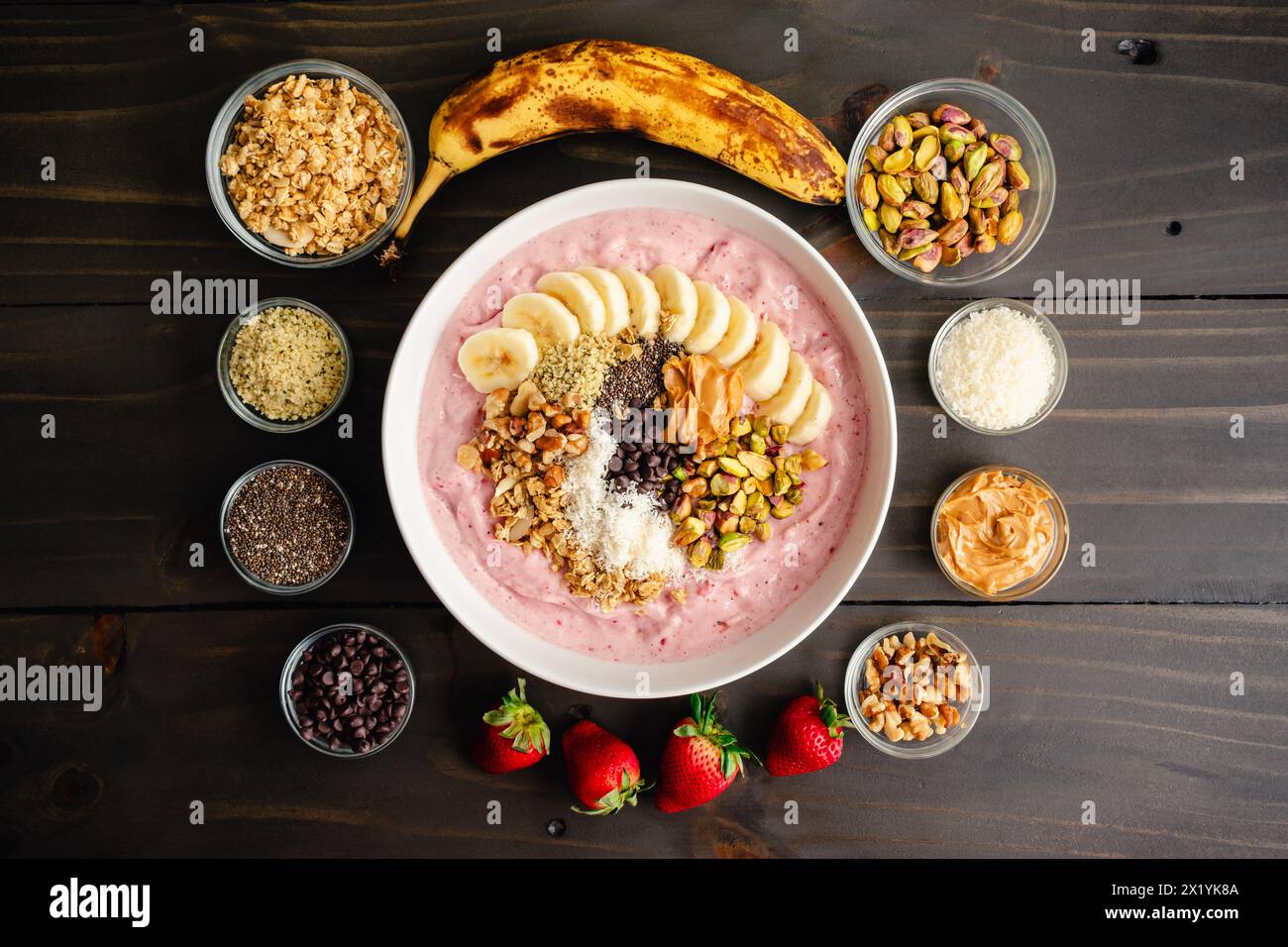 Erdbeere Smoothie Bowl voller gesunder Toppings: Fruchtige Schüssel mit Bananenscheiben, Samen, Nüssen, Erdnussbutter und dunklen Schokoladenchips Stockfoto