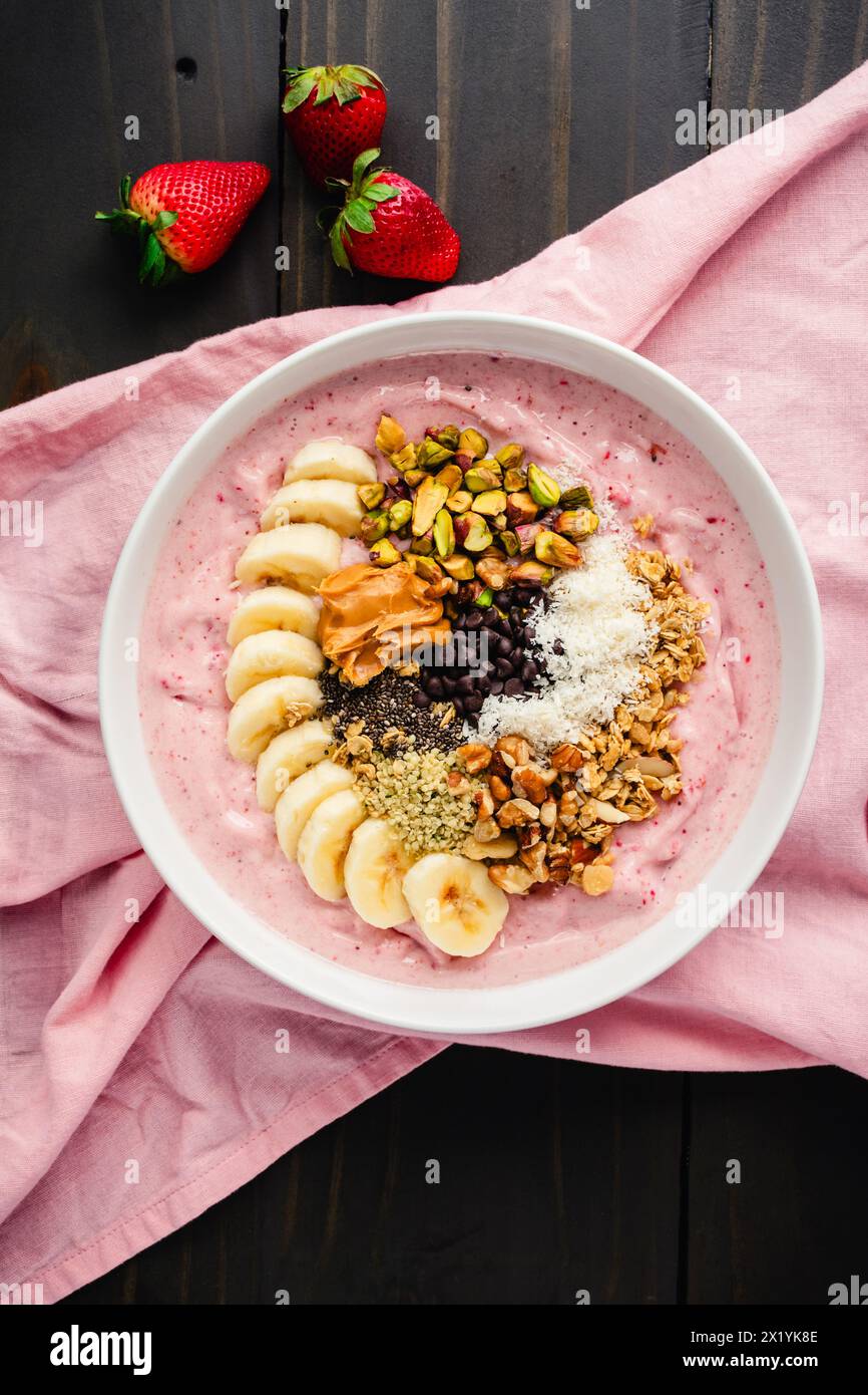 Erdbeere Smoothie Bowl voller gesunder Toppings: Fruchtige Schüssel mit Bananenscheiben, Samen, Nüssen, Erdnussbutter und dunklen Schokoladenchips Stockfoto