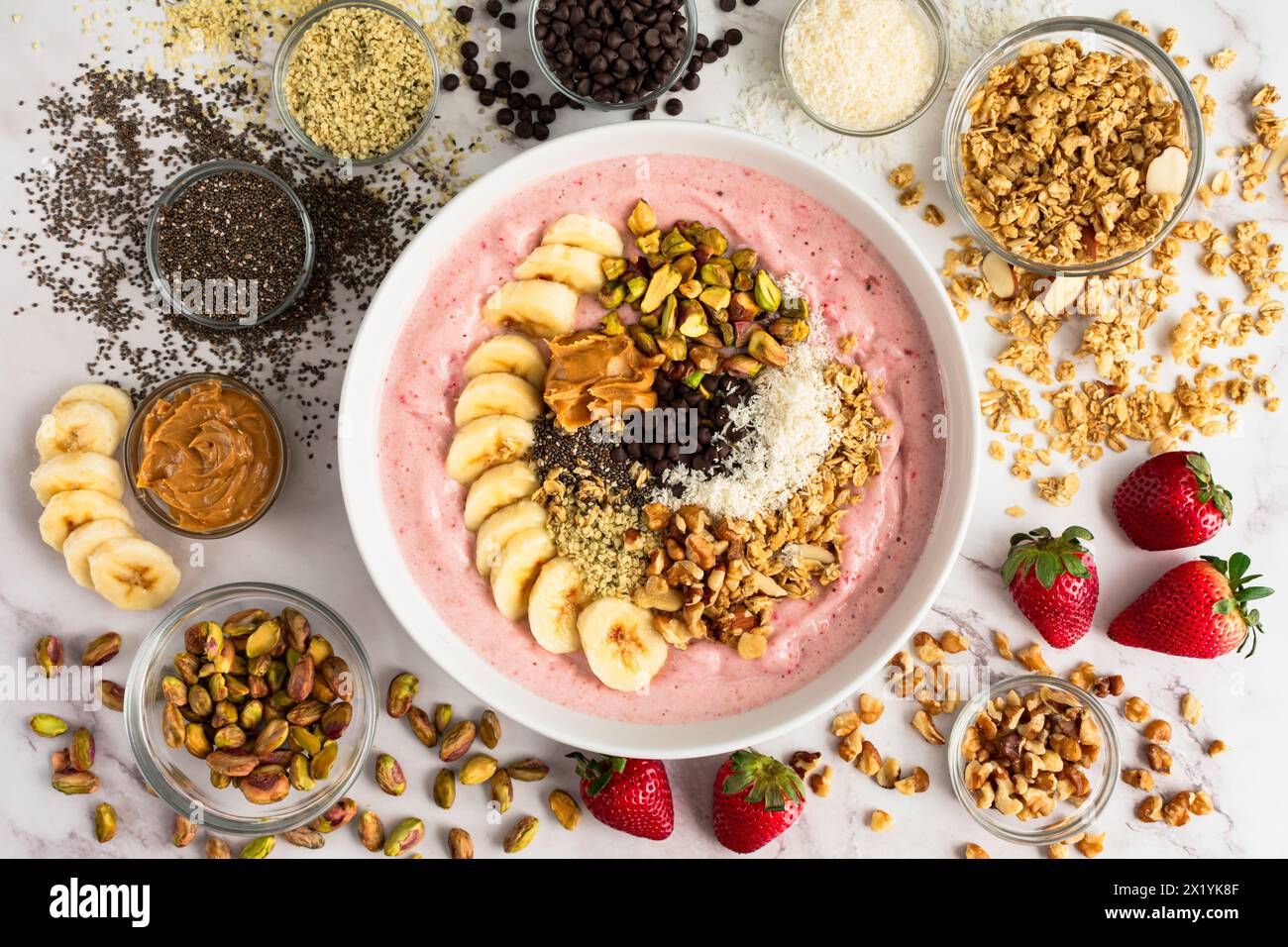 Erdbeere Smoothie Bowl voller gesunder Toppings: Fruchtige Schüssel mit Bananenscheiben, Samen, Nüssen, Erdnussbutter und dunklen Schokoladenchips Stockfoto