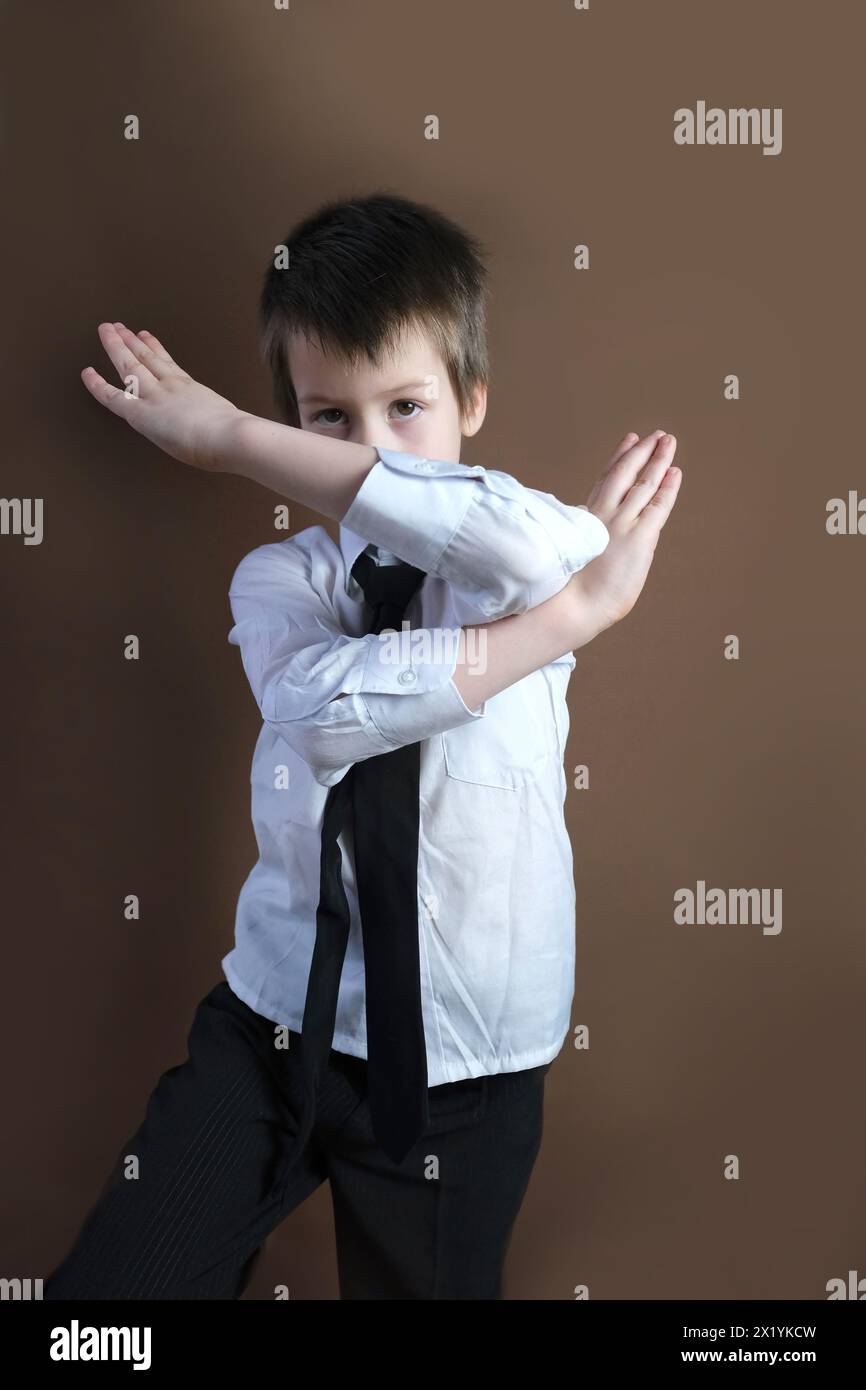 Kind 6-7 Jahre alt, Kind in weißem Business Hemd und Krawatte bedeckte sein Gesicht mit seinen Händen, formelle Uniform, Konzept eines jungen Geschäftsmannes, Performance Stockfoto