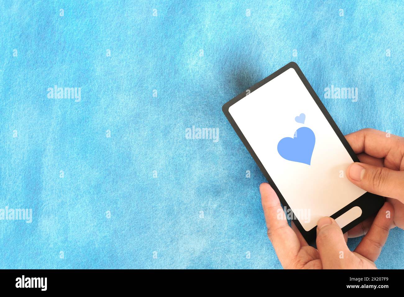 Menschliche Hand, die das Mobiltelefon mit blauem Herzsymbol hält. Freundlichkeit, Liebe und Positivität im Social-Media-Internet-Konzept. Stockfoto