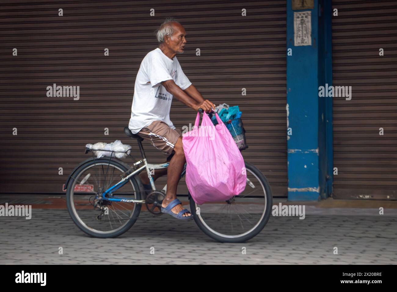 SAMUT PRAKAN, THAILAND, 16. März 2024, ein älterer Radfahrer mit großer Tasche fährt auf dem Bürgersteig entlang Stockfoto