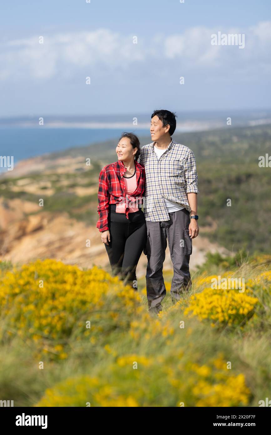 Ein Paar, das auf einem Hügel stand und einen wunderschönen Blick auf das Meer hatte. Der Mann trägt ein kariertes Hemd und die Frau ein rotes kariertes Hemd Stockfoto
