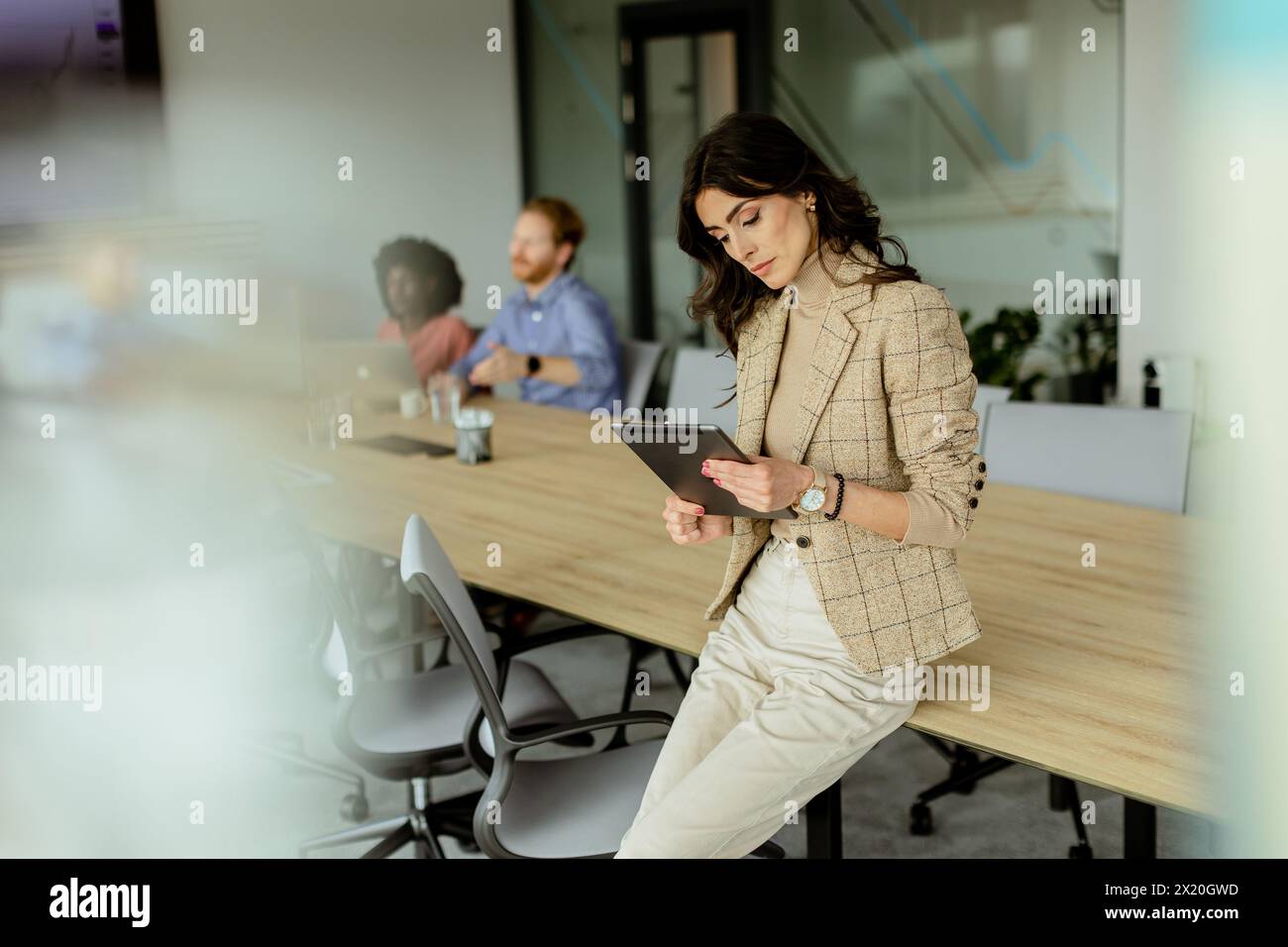 Eine kompetente Frau mit Tablet steht an der Spitze eines gemeinsamen Bürobereichs, ihr Team hat hinter ihr Diskussionen geführt. Stockfoto