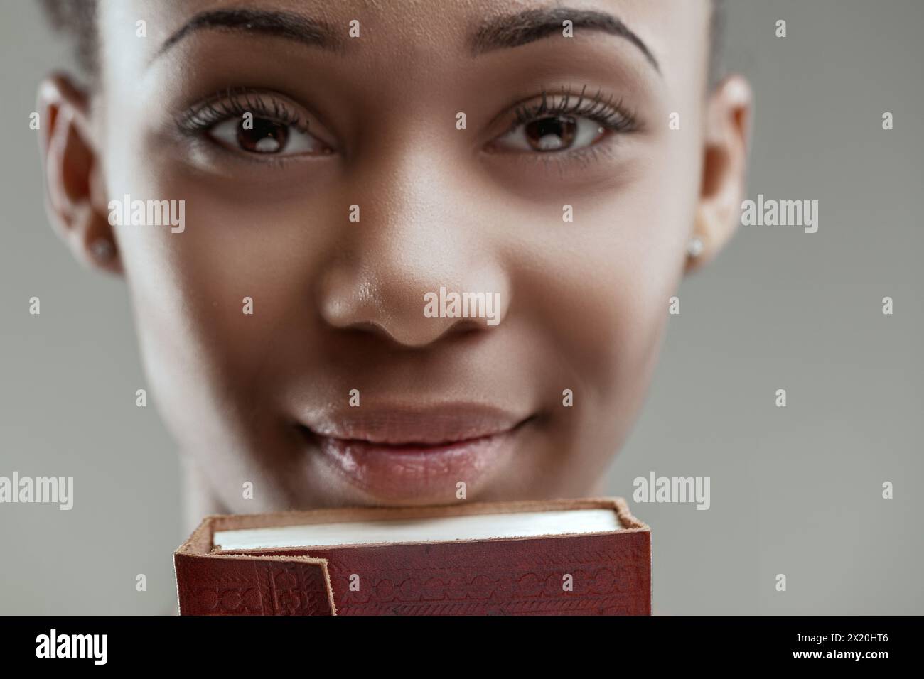 Eine junge Frau mit einem reich verzierten Tagebuch verdeckt teilweise ihr Gesicht, die Augen vermitteln stumme Geschichten Stockfoto