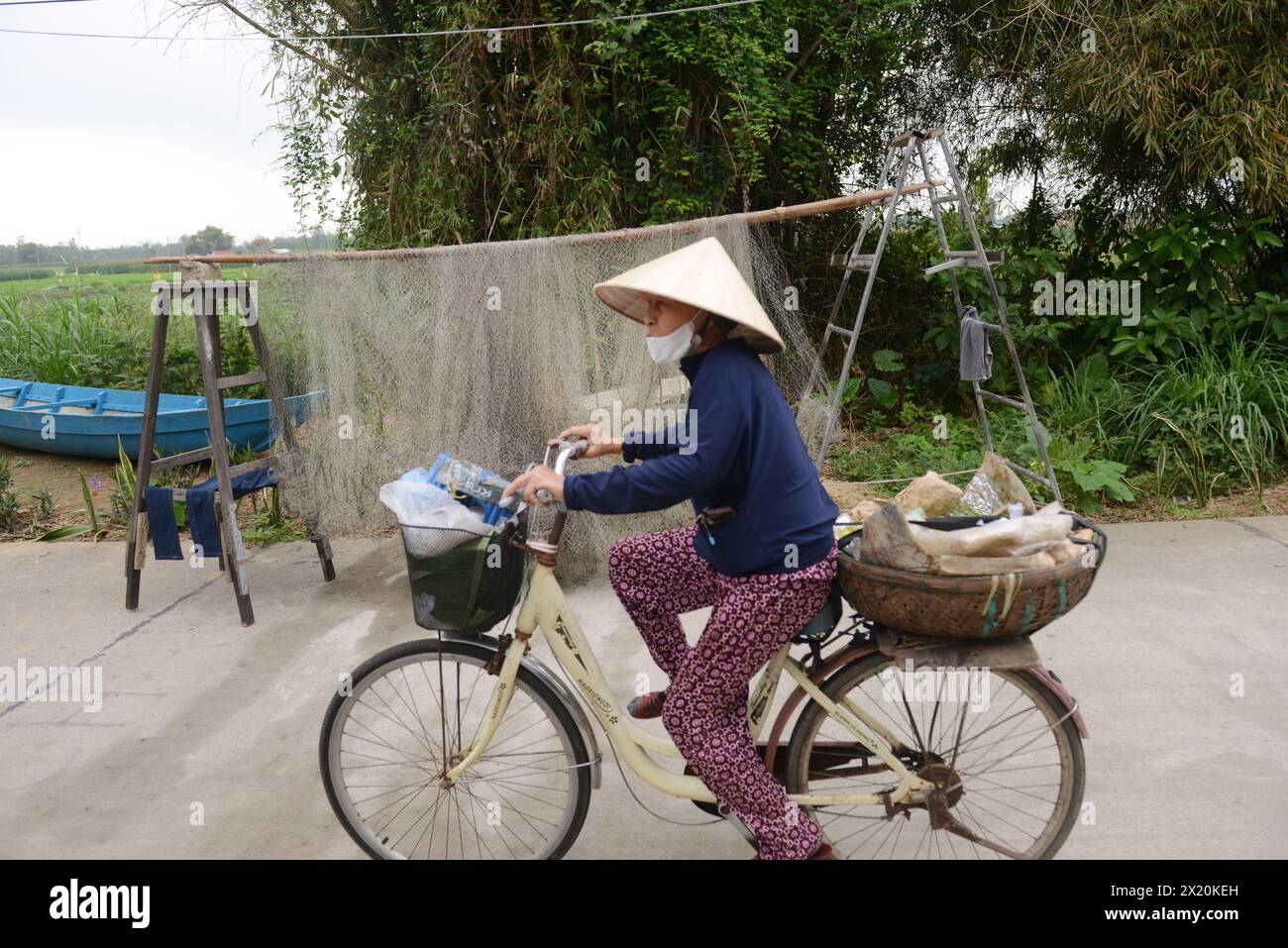 Eine vietnamesische Frau radelt durch ein großes Fischernetz in Bàn Thạch, Hoi an, Vietnam. Stockfoto