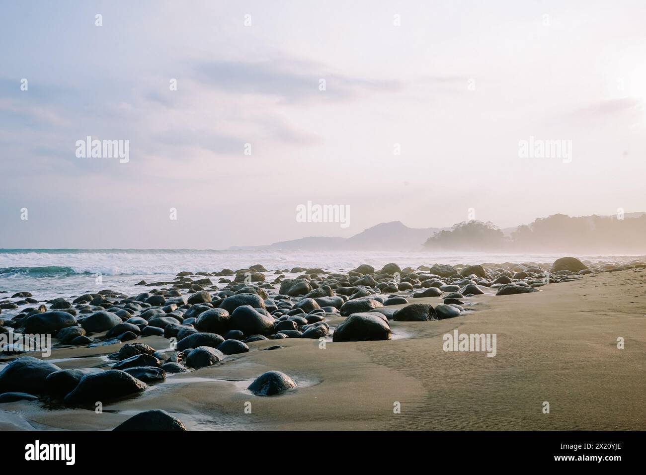 Die Ruhe am Morgen wird in einem ruhigen Küstenbild mit kleinen Wellen, felsigem Strand und der beruhigenden Aura des Sonnenaufgangs aufgenommen Stockfoto