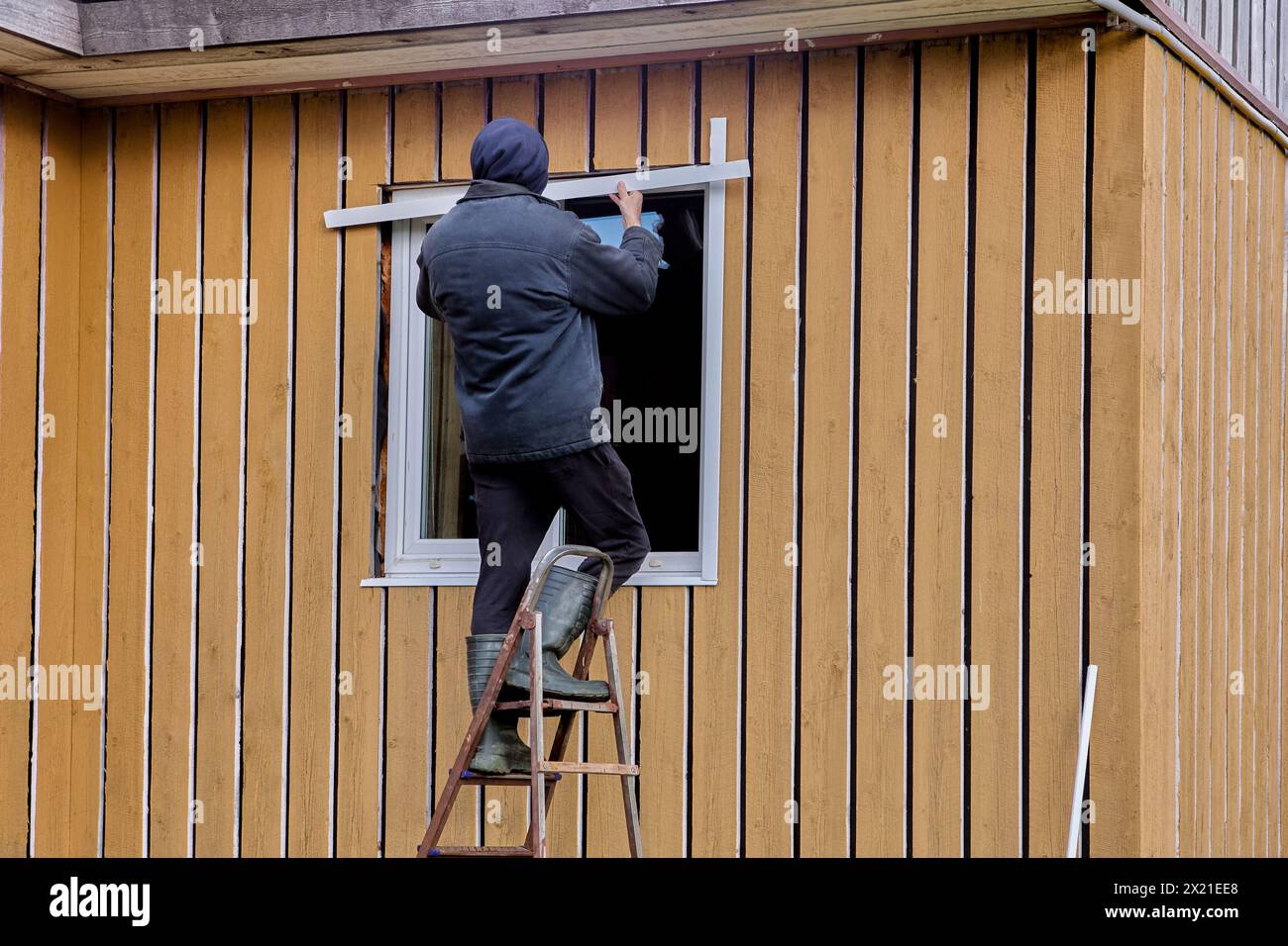 Außenfenster mit Metallverkleidungen und -Zierleisten, Bauarbeiter arbeiten auf der Trittleiter. Stockfoto