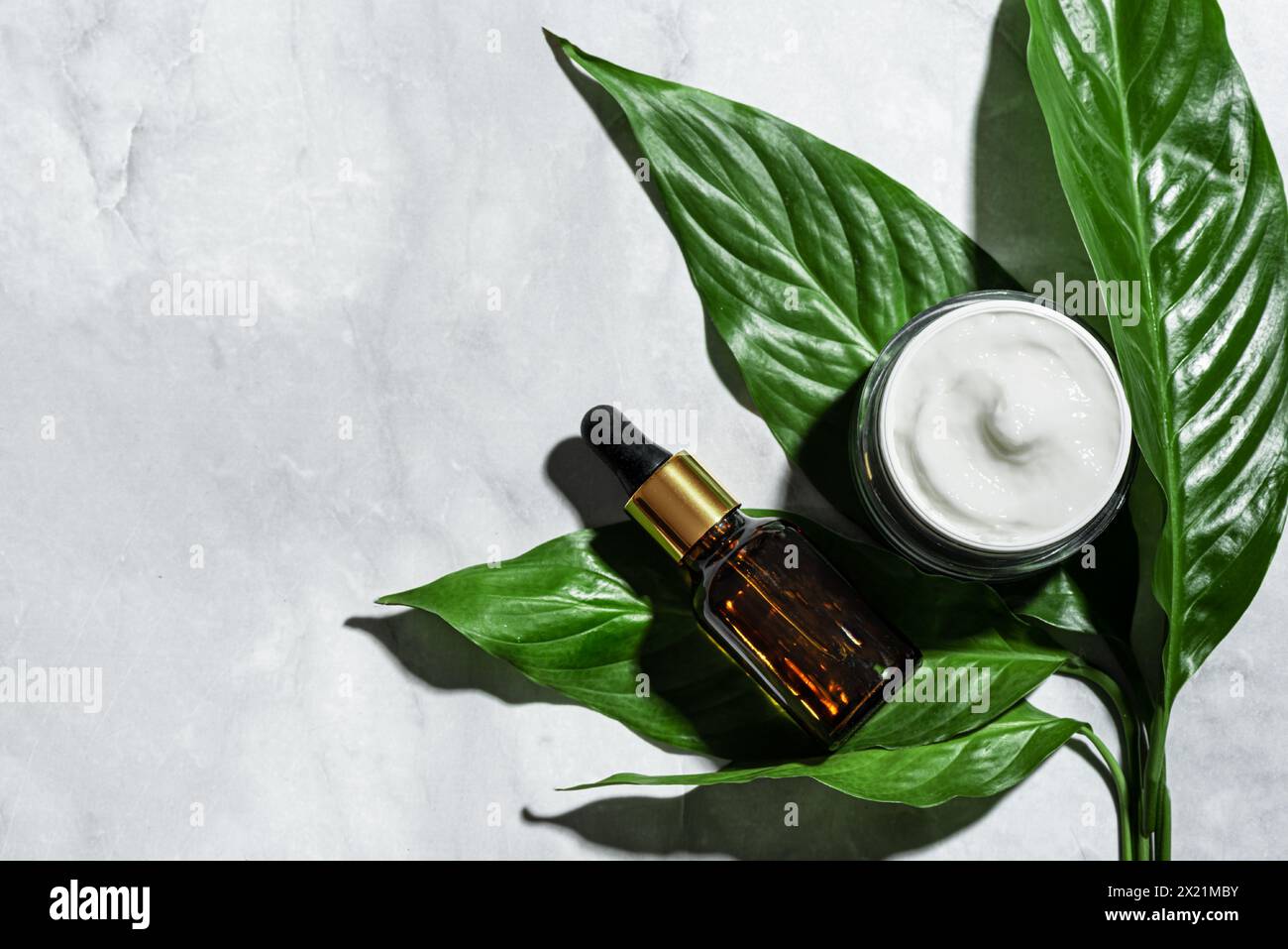 Natürliche Öko-Schönheit. Kosmetikprodukte und grüne Blätter auf Marmorhintergrund, Draufsicht, Kopierraum. Natürliches Bio-Hautpflegeserum und Gesichtscreme, er Stockfoto