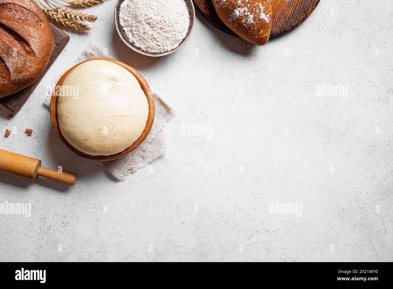 Schüssel mit frischem Hefeteig mit Mehl, Rollstift und frischem Sauerteigbrot auf weißem Hintergrund, Draufsicht, Kopierraum. Backen, Gebäck und Kneten Stockfoto