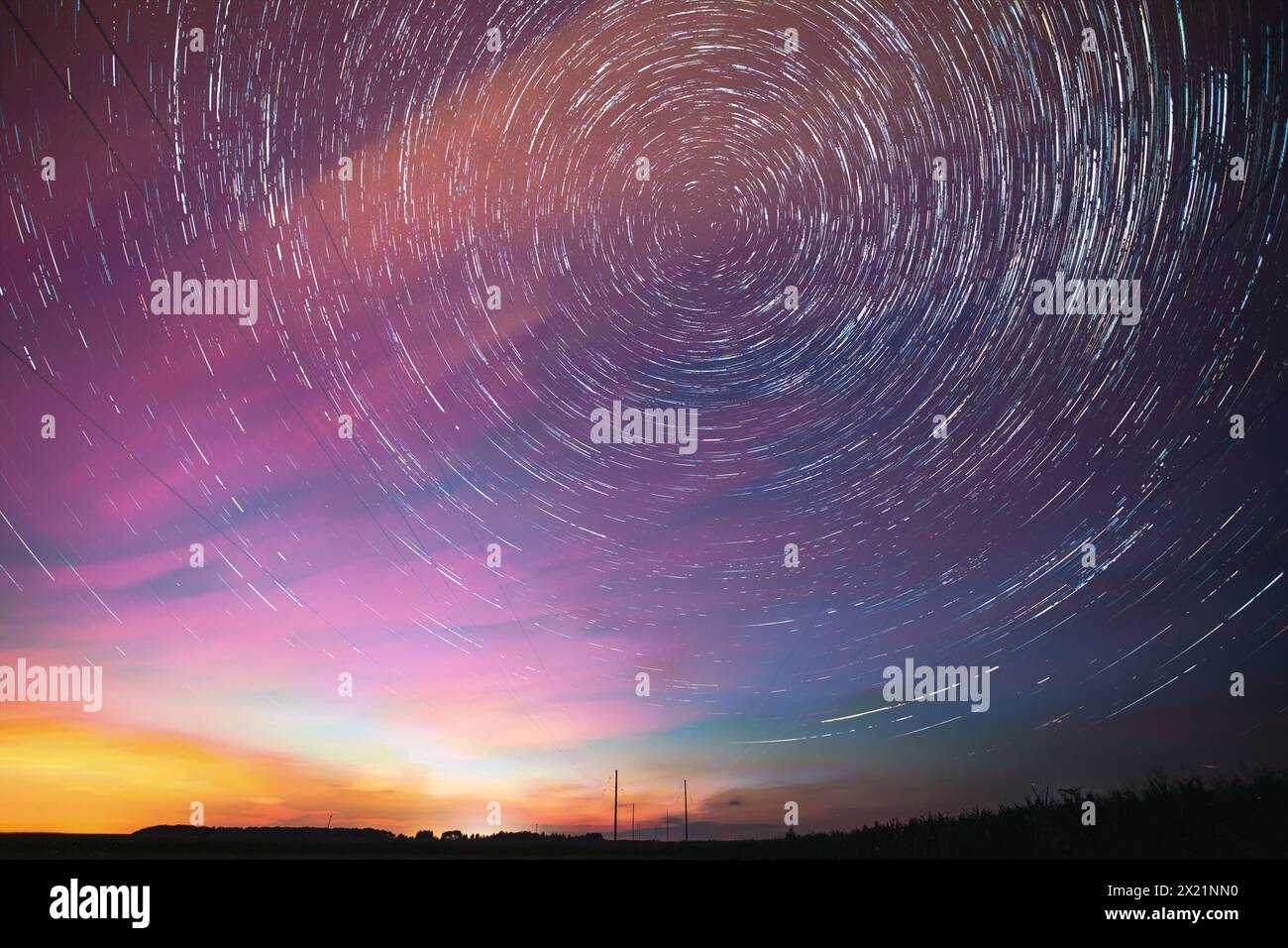 Heller Nächtlicher Sternenhimmel. Sanfte Blau-Orange-Rosa-Farben. Erstaunliche Sternenpfade Im Hintergrund Des Nachthimmels. Sternenspuren Über Der Stromleitung. Große Belichtung Stockfoto