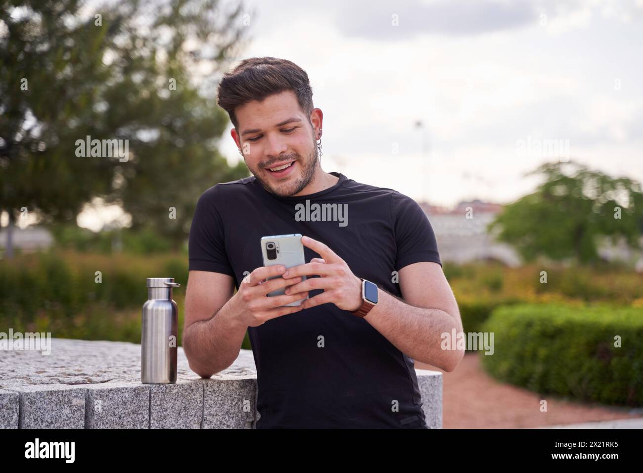 Porträt eines jungen, lächelnden Mannes, der mit seinen Freunden plaudert oder seine sozialen Netzwerke mit seinem Smartphone ansieht Stockfoto