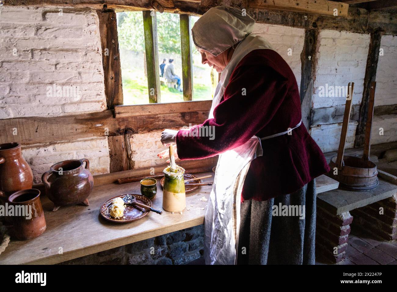 Frau, die Butter in einem mittelalterlichen Häuschen aufwirbelt, Weald & Downland Living Museum, West Sussex, England Stockfoto