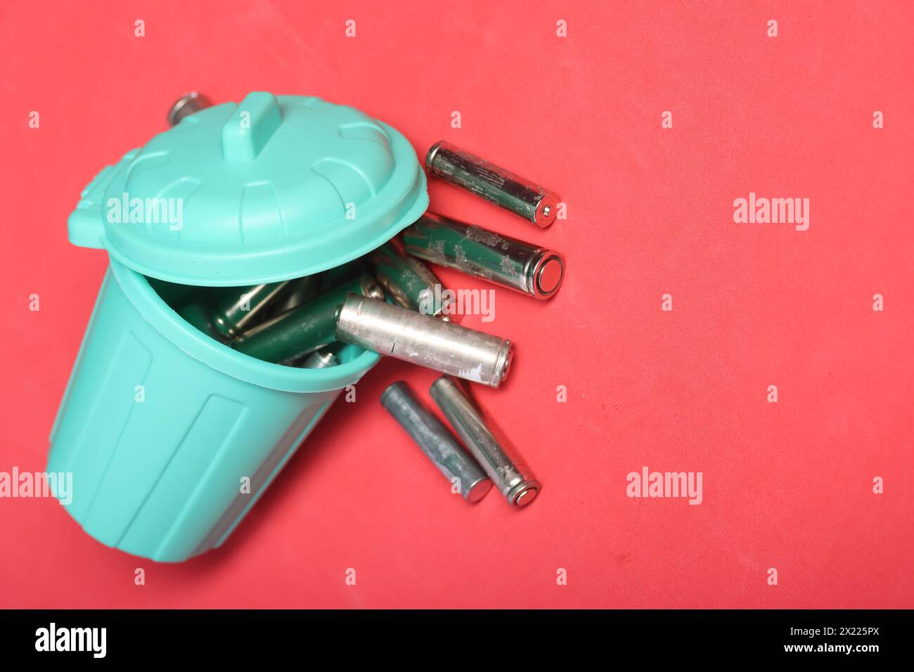 Gebrauchte Fingerbatterien in einem Miniatur-Mülleimer. Rosafarbener Hintergrund. Feld für Text. Stockfoto