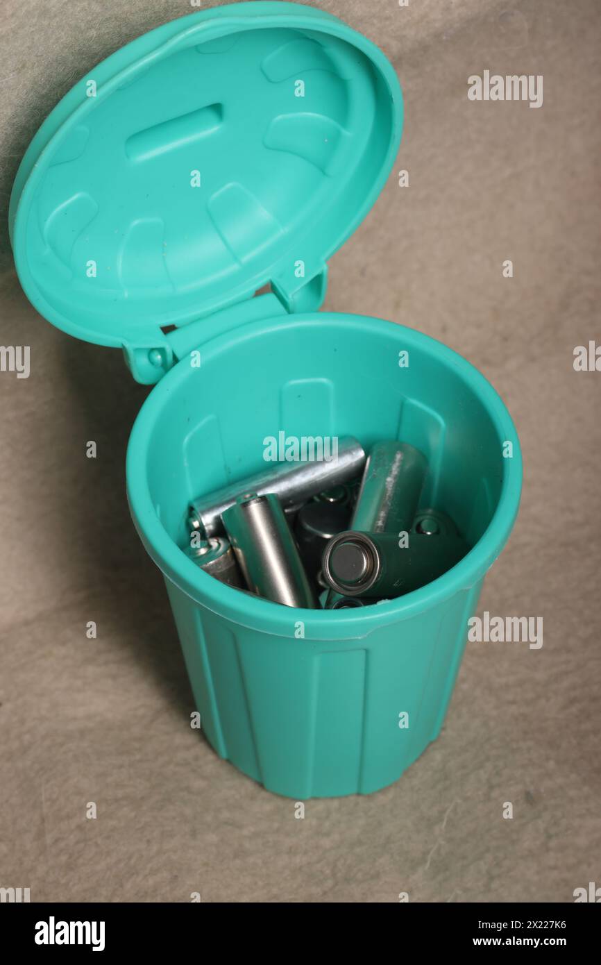 Gebrauchte Fingerbatterien in einem Miniatur-Mülleimer. Auf einem beigefarbenen schmutzigen Hintergrund. Stockfoto
