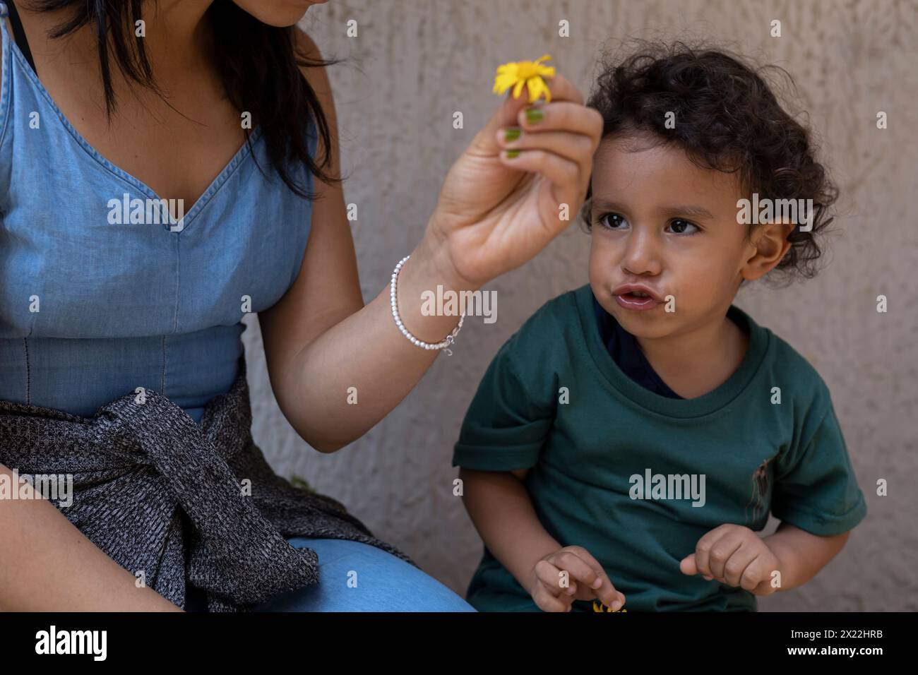 Lateinamerikanische Mutter und ihr Sohn spielen mit einer gelben Blume. Mutterschaft und Muttertagskonzept. Stockfoto