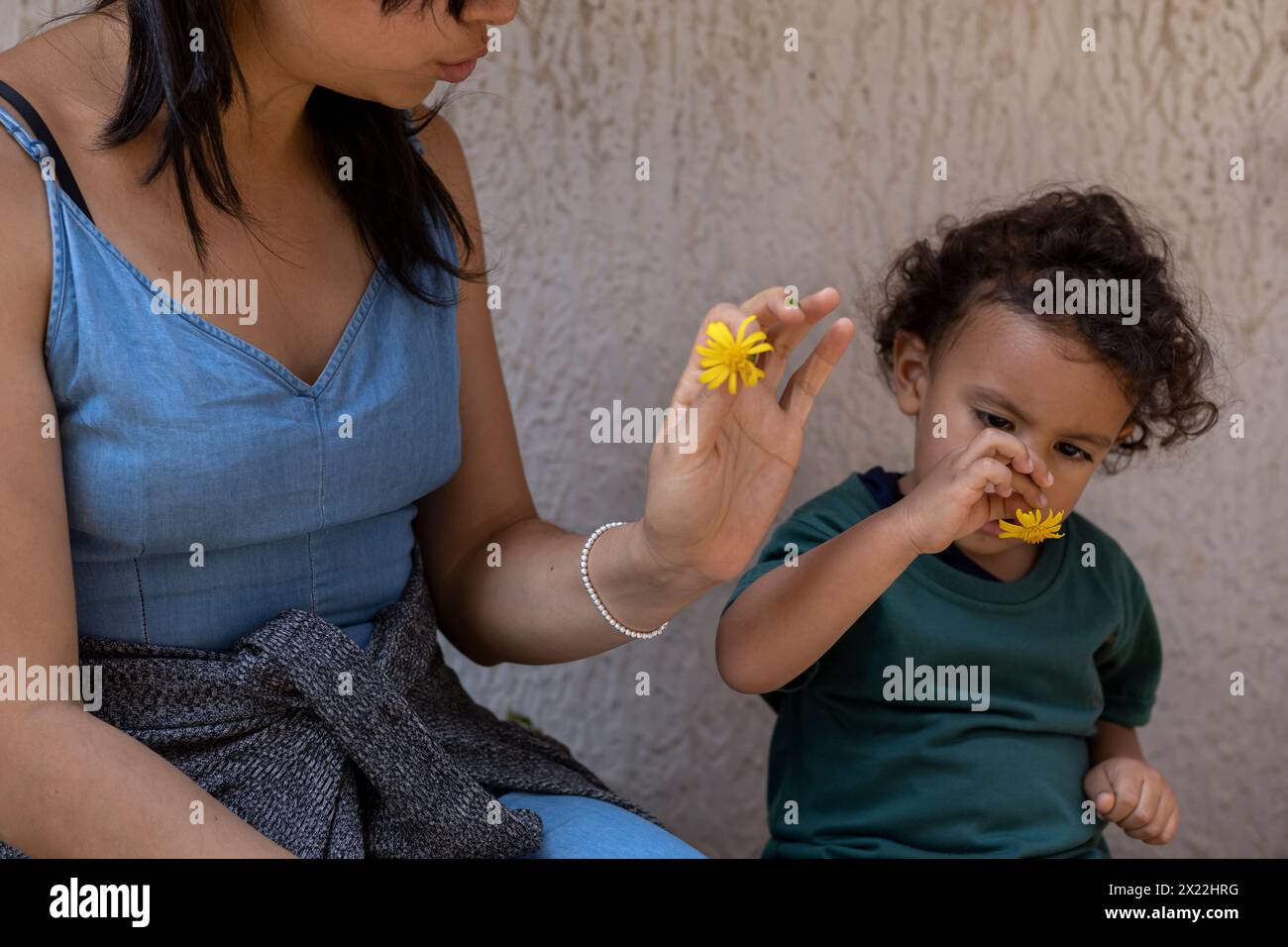 Lateinamerikanische Mutter und ihr Sohn spielen mit einer gelben Blume. Mutterschaft und Muttertagskonzept. Stockfoto
