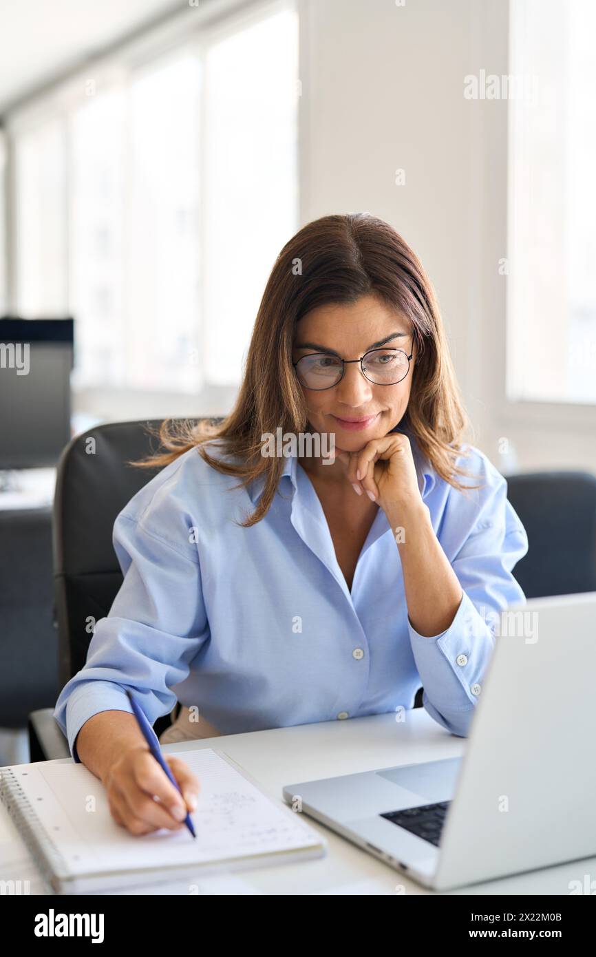 Beschäftigte Geschäftsfrau mittleren Alters, die am Laptop arbeitet, im Büro Schreibzettel. Stockfoto