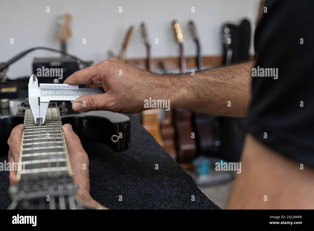 Der lateinamerikanische Geigenbauer kalibriert die Saiten einer elektrischen Gitarre mit einem Nonius. Person nicht erkennbar. Gitarrenkonzept, Kalibrierung, ins Stockfoto