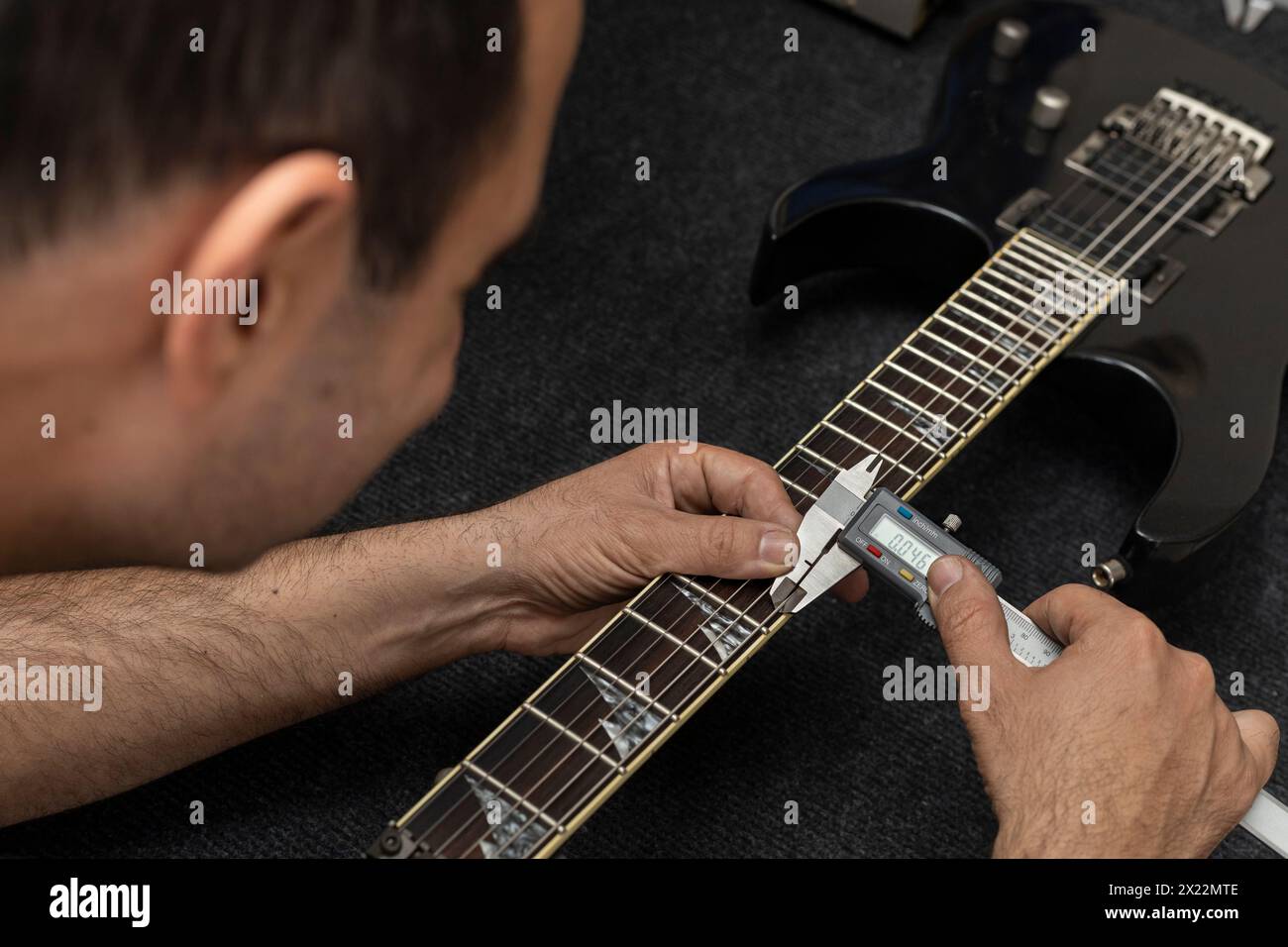 Lateinamerikanischer Geigenbauer kalibriert die Saiten einer elektrischen Gitarre mit einem digitalen Nonius. Nicht Erkennbar. Gitarrenkonzept, Kalibrierung, Instrument. Stockfoto