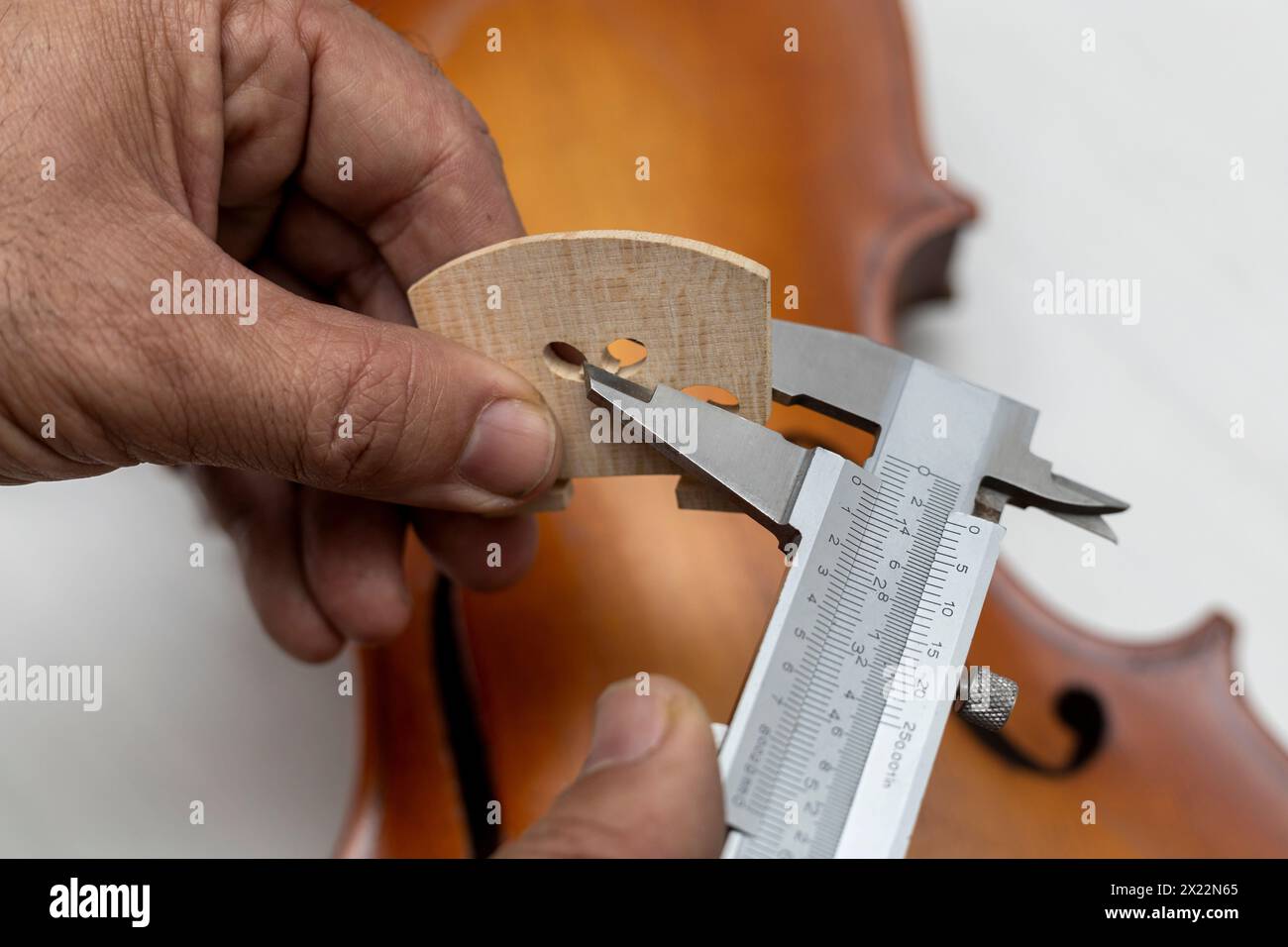 Hände eines nicht erkennbaren lateinamerikanischen Geigenbauers, der präzise Messungen einer Geigenbrücke mit einem Nonius macht. Konzeptinstrumente Stockfoto
