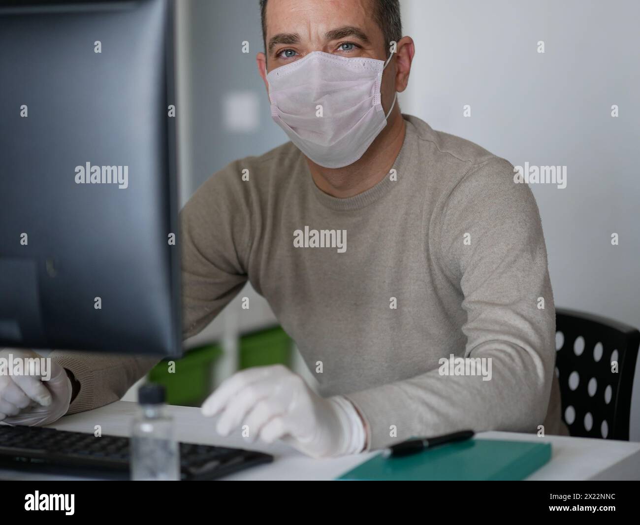 Junge Frau mit Schutzhandschuhen an den Händen und Maske auf dem Gesicht, die vom Büro oder zu Hause aus mit dem Laptop auf dem Schreibtisch arbeitet. Zur Verhinderung des Coronavirus covid-19 spr Stockfoto