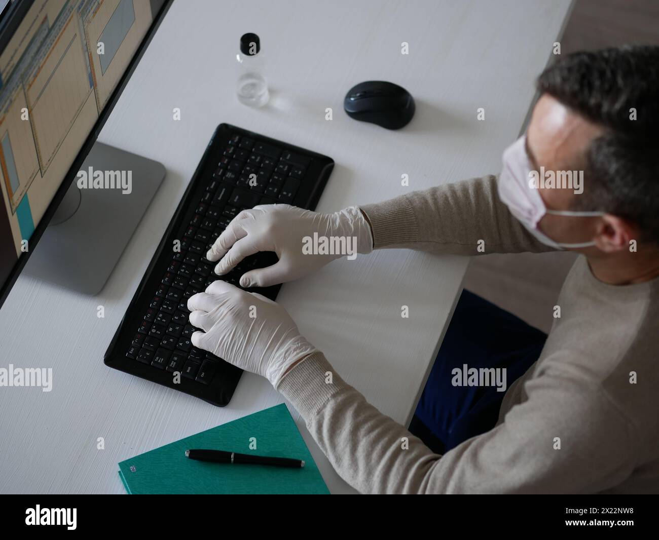 Junge Frau mit Schutzhandschuhen an den Händen und Maske auf dem Gesicht, die vom Büro oder zu Hause aus mit dem Laptop auf dem Schreibtisch arbeitet. Zur Verhinderung des Coronavirus covid-19 spr Stockfoto