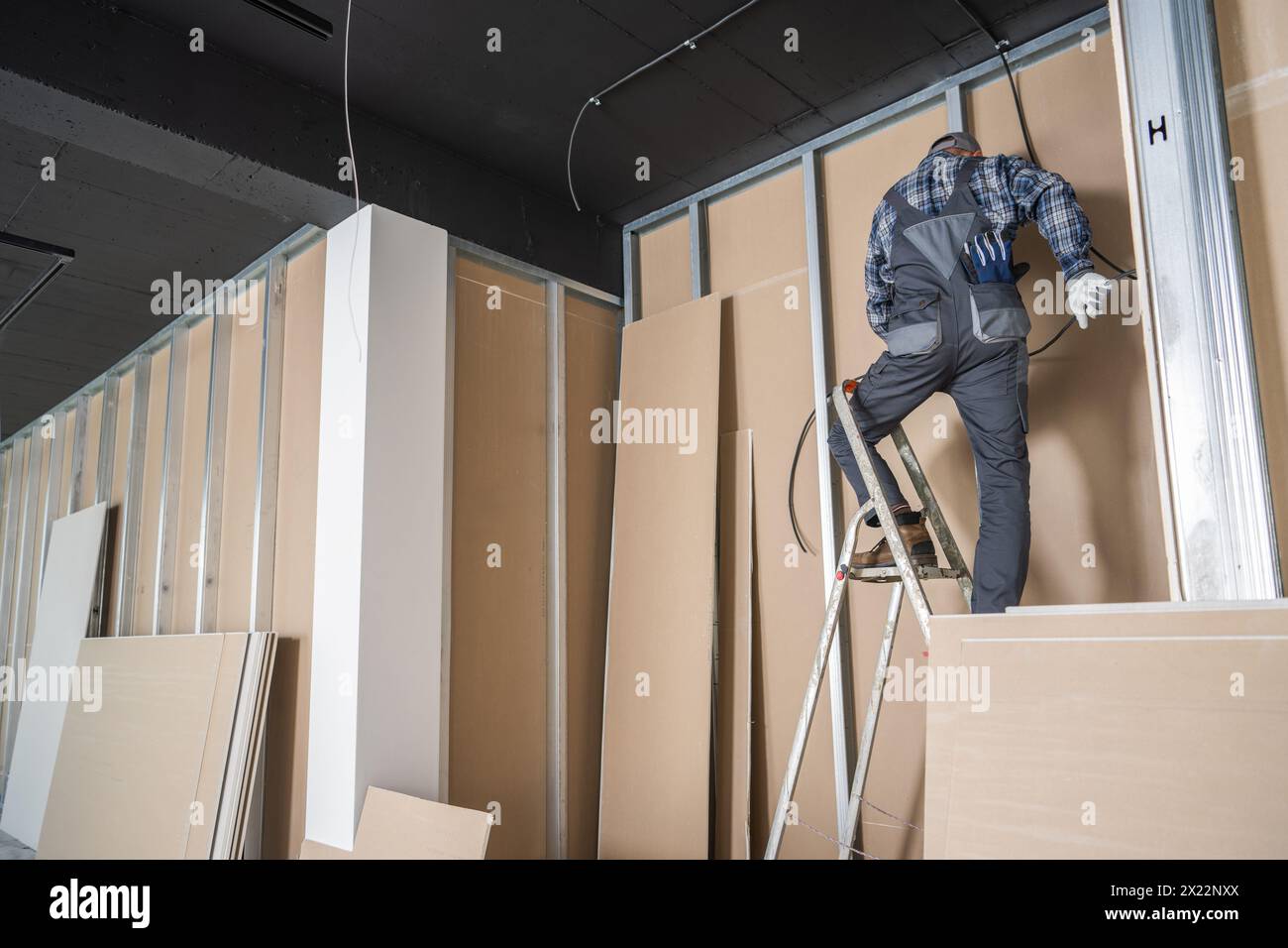 Elektriker, der ein Elektrokabel installiert, während er auf einer Leiter steht. Innenausstattung. Stockfoto