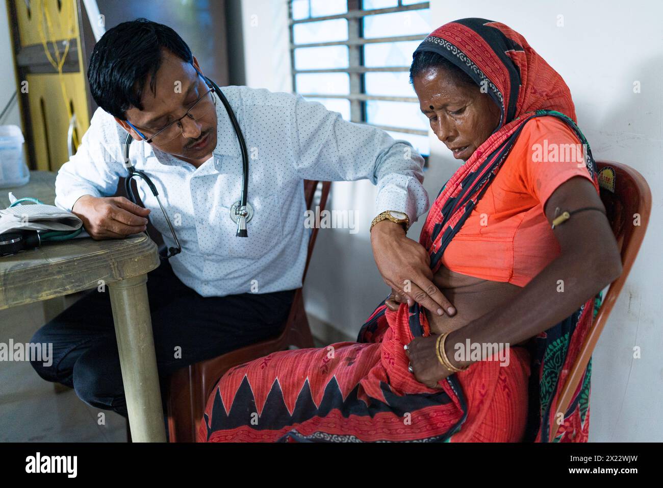 Kalkutta, Indien - 29. Oktober 2024: Ein indischer Arzt wird in einer Klinik auf dem Land gesehen, wie er eine alte Patientin berät und Medikamente verschreibt Stockfoto