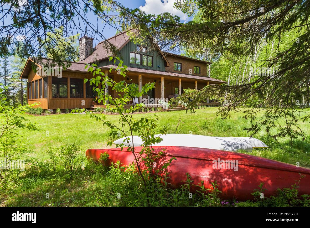Rückansicht von braun und grün gebeiztem Fichtenholz und Zedernschindel, das LEED-zertifiziertes Landhaus mit Veranda im späten Frühjahr in Quebec, Kanada Stockfoto