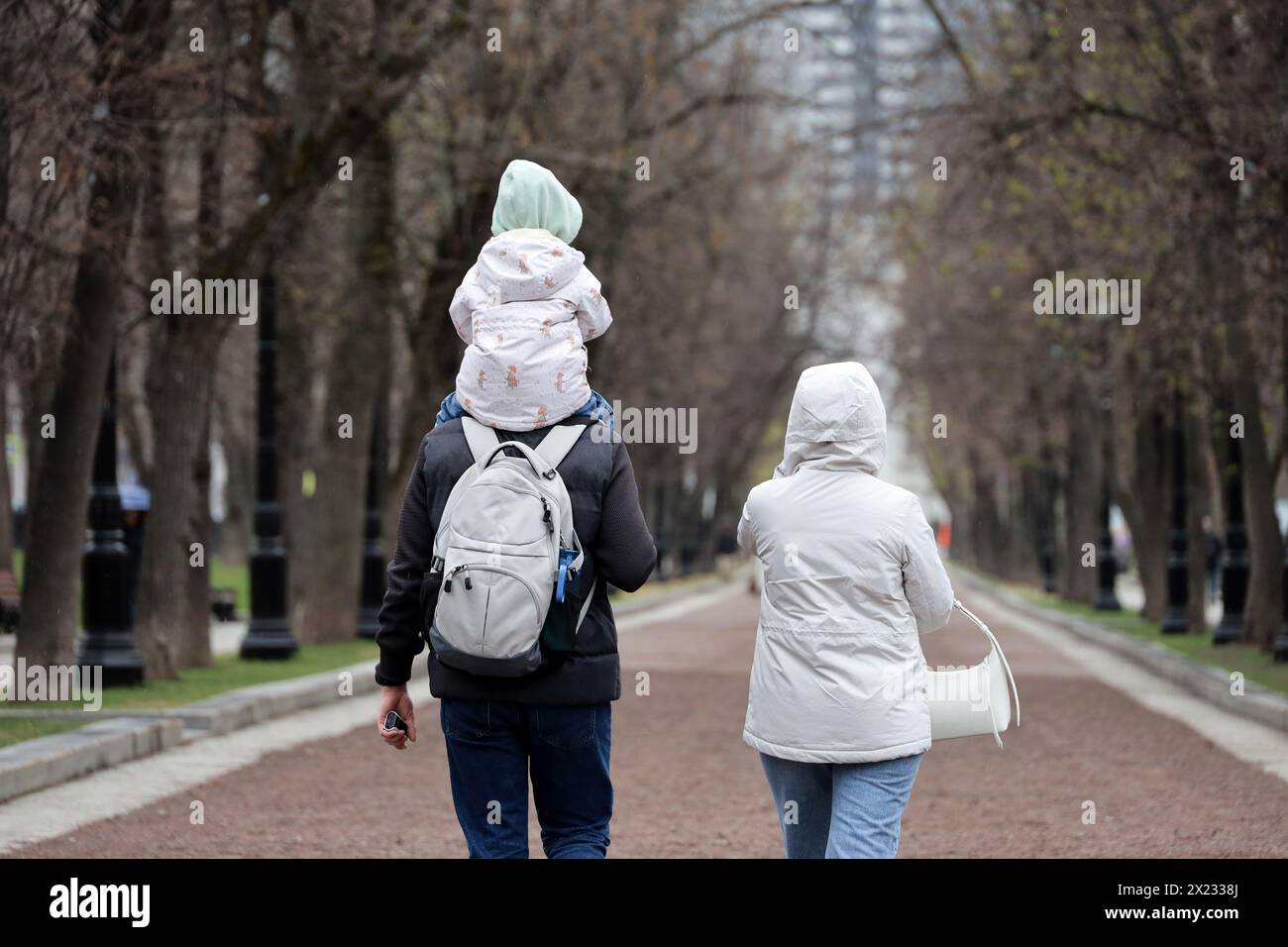 Paare mit Kind, die im Frühjahr auf einer Straße in der Stadt spazieren gehen. Vater mit Kind, das auf seinen Schultern sitzt Stockfoto
