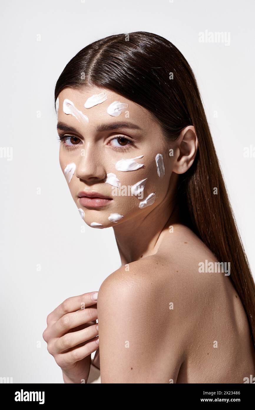 Eine schöne junge Frau posiert mit ätherischer weißer Creme auf ihrem Gesicht und zeigt einzigartige und künstlerische Make-up-Techniken. Stockfoto