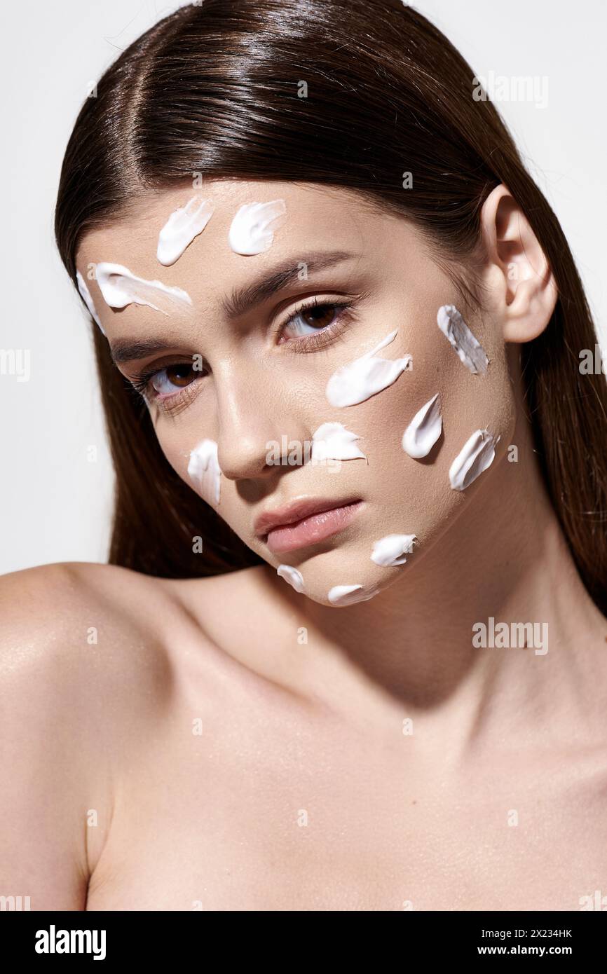 Eine schöne junge Frau posiert mit weißer Creme auf dem Gesicht und kreiert einen einzigartigen und künstlerischen Look. Stockfoto