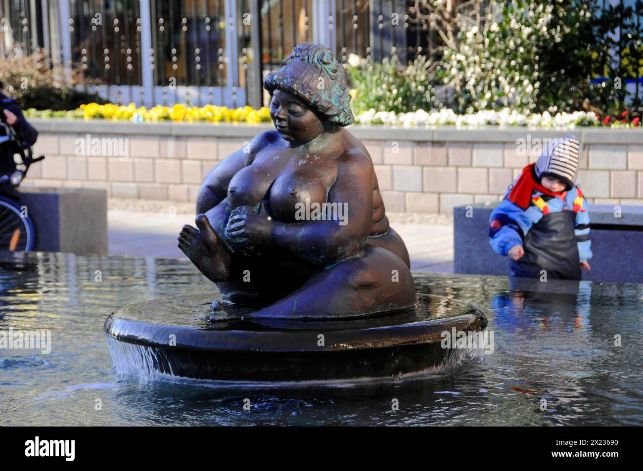 Brunnenfigur Wilhelmine, Wahrzeichen von Westerland, Westerland, Bronzeskulptur einer sitzenden Frau in einem Brunnen, ein Kind, das im Hintergrund spielt Stockfoto