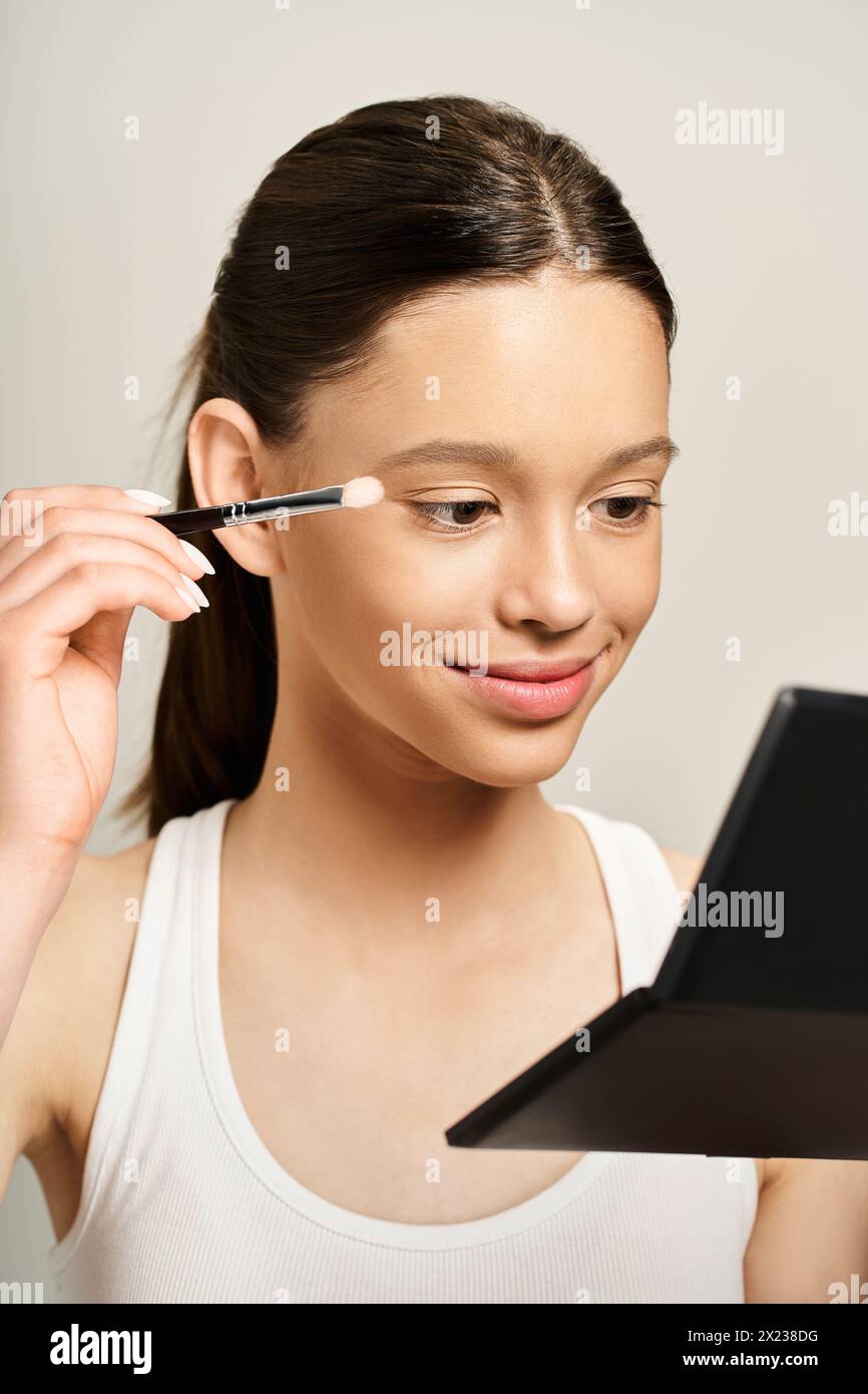 Ein stilvolles Mädchen im Teenageralter, das mit einem Pinsel ein Make-up auf das eigene Gesicht aufträgt und eine lustige und künstlerische Form des Selbstausdrucks zeigt. Stockfoto