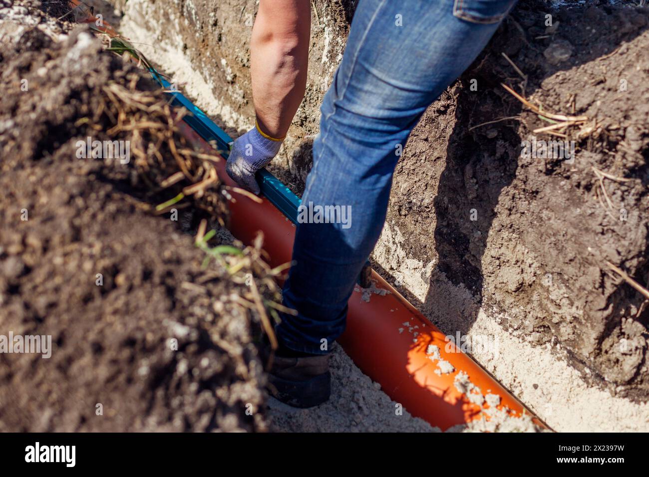 Klempnermessung der Steigung montierter Abwasserrohre mit Wasserwaage im Graben. Haus bauen. Mitarbeiter prüft Pipeline Stockfoto