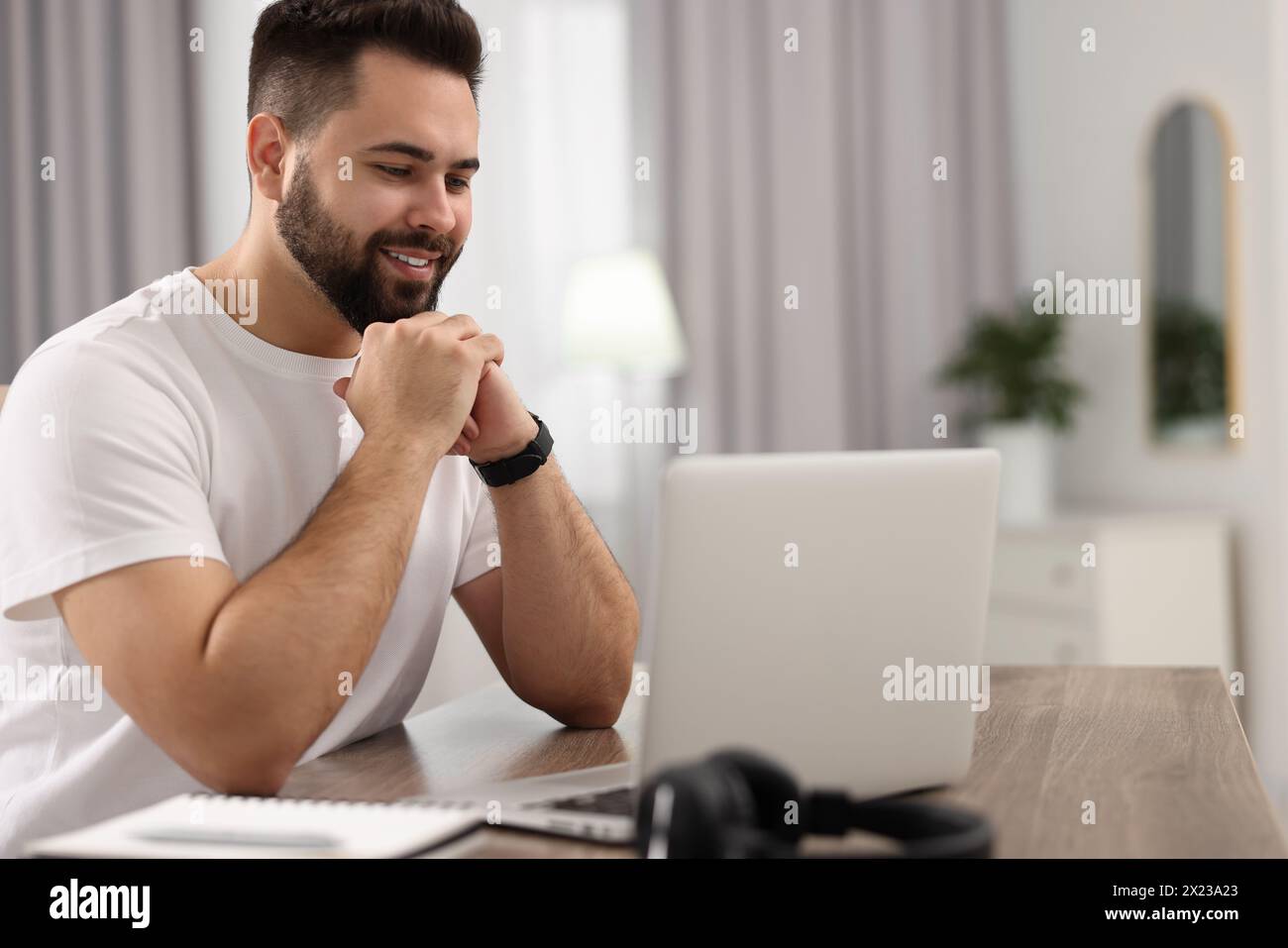 Junger Mann, der sich ein Webinar am Tisch im Zimmer ansieht Stockfoto
