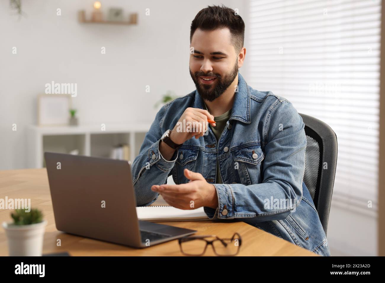 Junger Mann, der Videochat während des Webinars am Tisch im Zimmer nutzt Stockfoto