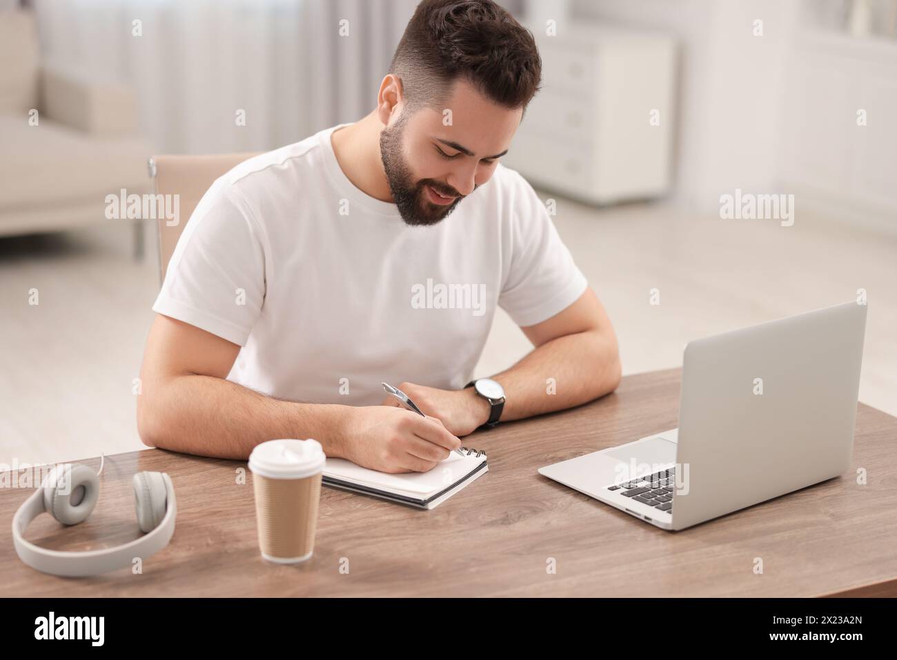 Junger Mann, der sich während des Webinars am Tisch im Raum Notizen macht Stockfoto