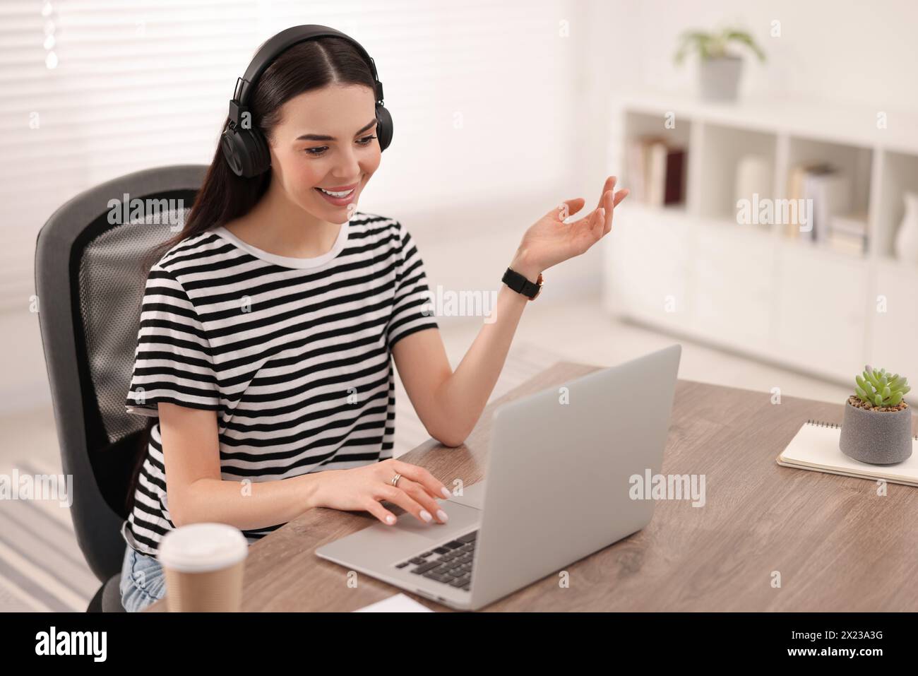 Junge Frau in Kopfhörern, die während des Webinars am Tisch im Zimmer Videochat nutzt Stockfoto