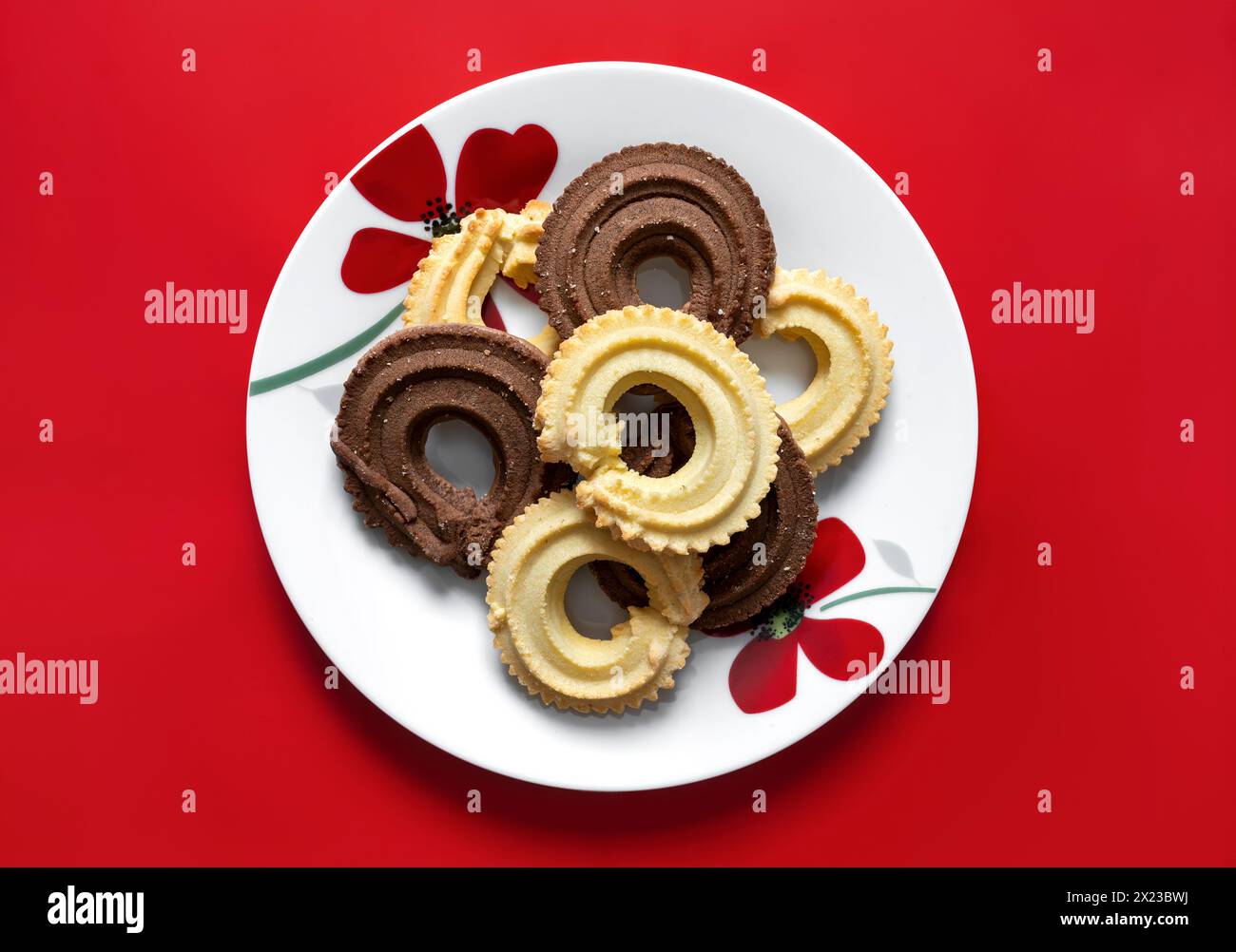 Wiener Strudel-Kekse mit Schokolade und Vanille auf weißem Teller mit rotem Blumenmuster auf rotem Hintergrund Stockfoto