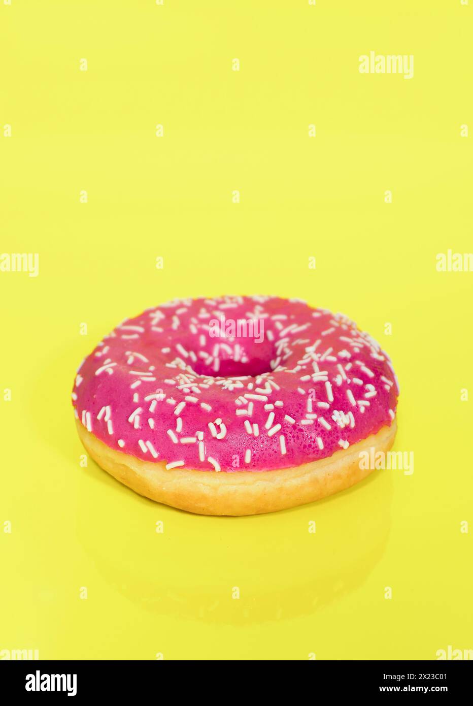Pink Iced Ring Donut mit Streuseln auf einem gelben Hintergrund Stockfoto