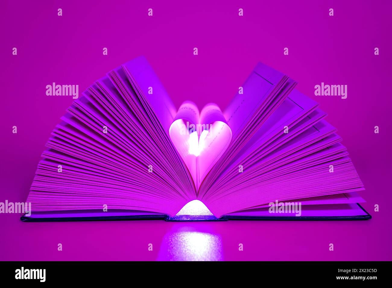 Öffnen Sie das Buch auf rosa/lila Hintergrund mit den mittleren Seiten, die in Herzform umgewandelt werden Stockfoto